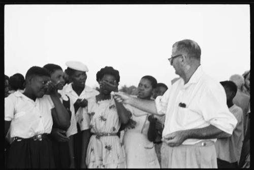 Group of people standing with C.J. Mathias, who is holding something out to a group of women
