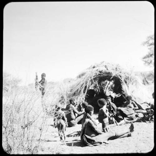 People sitting in front of the skerm of "Old ≠Toma" and /Gam, with a man holding a piece of meat near them