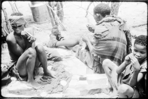 Dadum sitting on animal skins with her husband, Tama, and an unidentified boy. Tama is sewing. (copy of color slide 2001.29.8359)