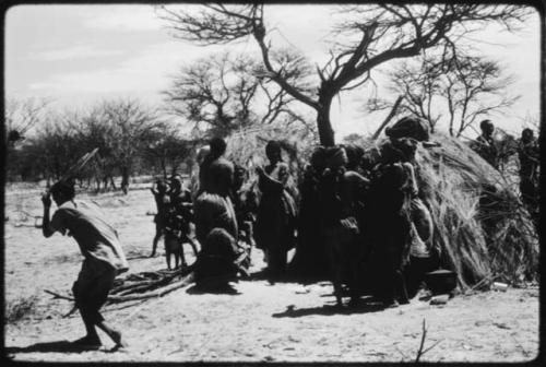 Women performing the Eland Dance, with some standing in front of a skerm, singing and clapping, and others dancing around the skerm (copy of color slide 2001.29.8649)