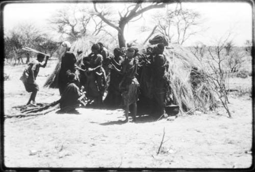 Women performing the Eland Dance, with some standing in front of a skerm, singing and clapping, and others dancing around the skerm (copy of color slide 2001.29.8650)