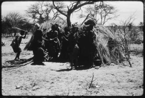 Women performing the Eland Dance, with some standing in front of a skerm, singing and clapping, and others dancing around the skerm (copy of color slide 2001.29.8650)