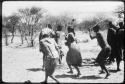 People performing the Eland Dance, with Twi imitating the sideways motion of an eland's hind legs and playing up to ǂKxoba (copy of color slide 2001.29.8657)