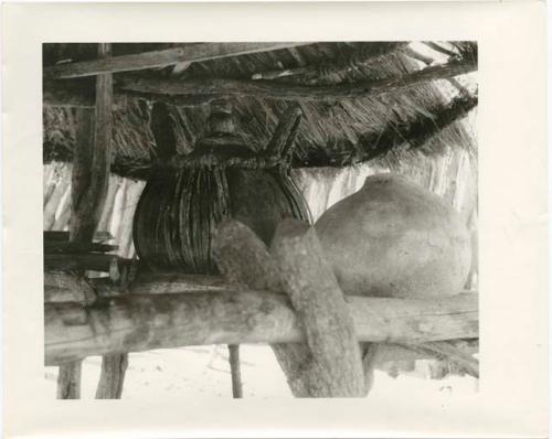 Churns under a thatched roof (print is a cropped image)