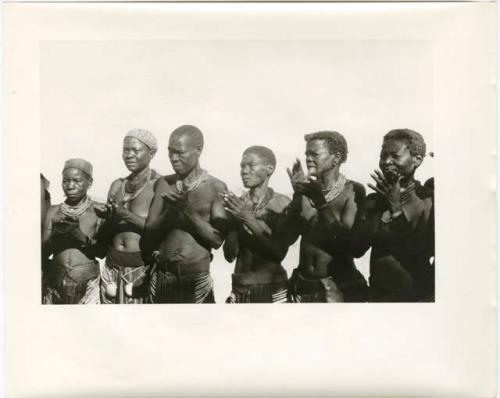 Women standing in a semi-circle, clapping for a dance (print is a cropped image)