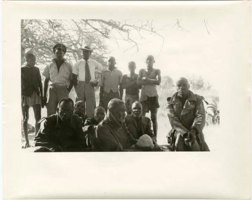 Group of men sitting and standing, all wearing Western clothing (print is a cropped image)