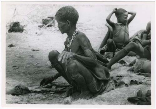 "Old Xama" poking a fire with a stick, with unidentified people to the right (print is a cropped image)