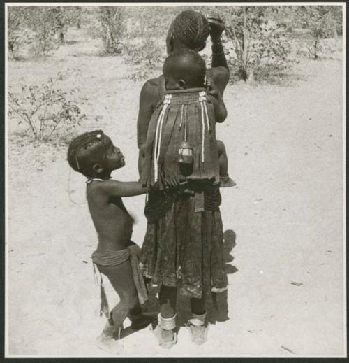 Woman carrying a child on her back, and another child standing next to her