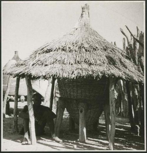 Person sitting next to a storage basket covered with a thatched roof