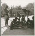 Girls sitting and working on a woven band with beads on it, and a woman standing next to them