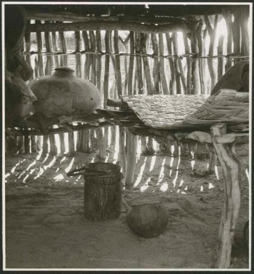 Woven mat, wooden bucket with leather handle, and large pot inside a storage hut