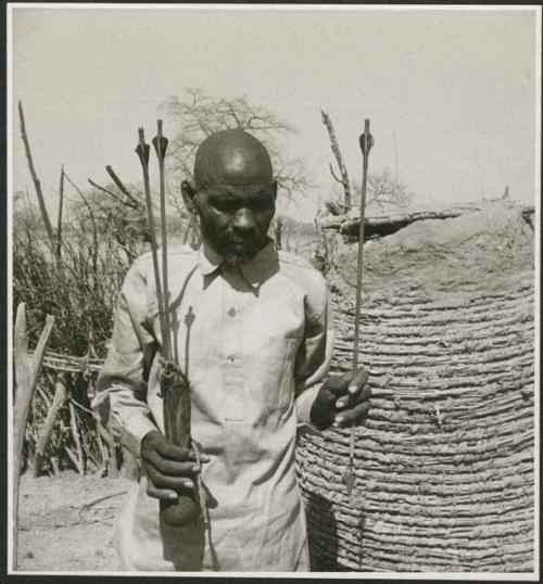 Man holding arrows with metal points and feathered ends, two of them in a quiver