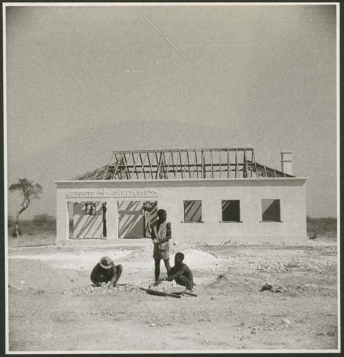 Men sitting and standing in front of a clinic under construction