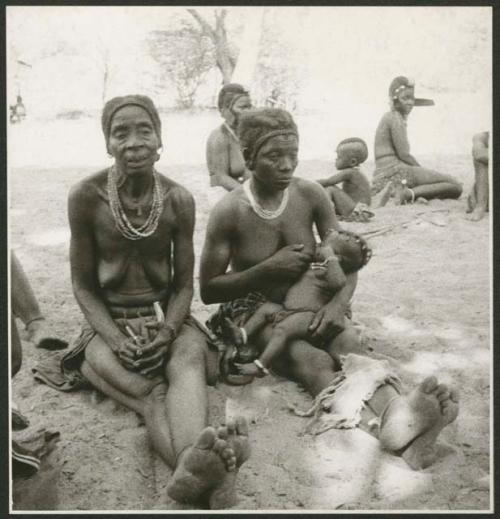 Two women sitting, and one is nursing a child