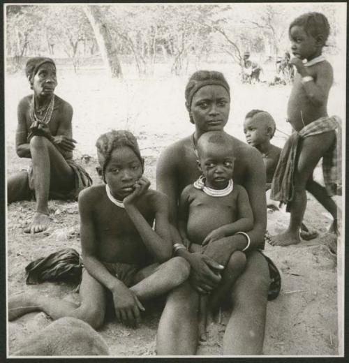 Women sitting, with children sitting and standing near them