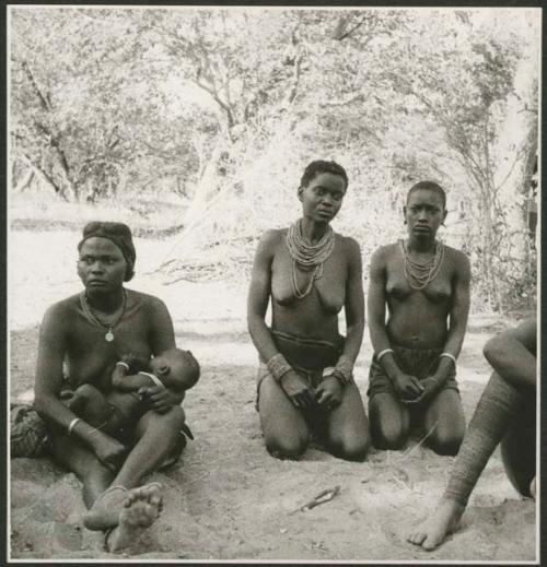 Woman sitting and nursing a baby, and two women kneeling