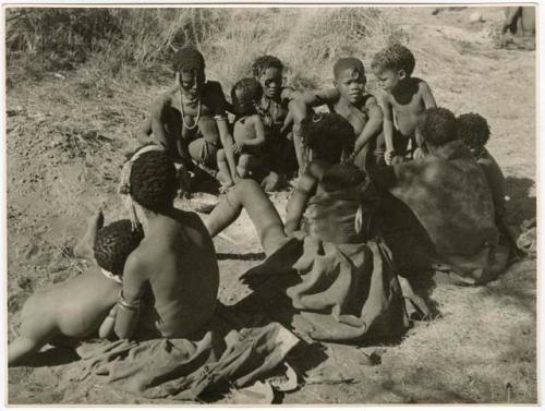 /Naoka, first wife of /Ti!kay, performs a choa ceremony for her daughter, Bau, wife of Tsamgao. N!ai, /Naoka's sister; !Ghia, wife of ≠Gao; and Goishay, mother of /Naoka and N!ai are seated with their backs to the camera watching (print is a cropped image)