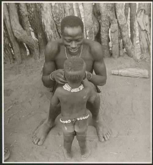 Man sitting, with a child standing in front of him