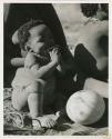 Baby sitting next to an ostrich eggshell (print is a cropped image)