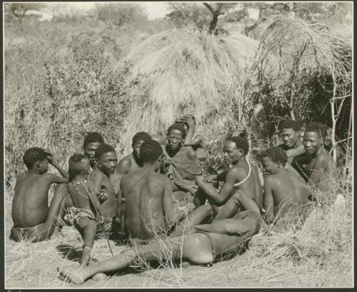 Group of Ju/'hoansi telling stories including left to right: "Lame ≠Gao" seen from behind, ≠Gao (Khwo//o-/Gasa's husband), "Gao Medicine," unidentified person seen from behind, ≠Toma, !Naishi, "Old Xama" with her hands over her head, "Gao Helmet" in profile, "Old Demi" lying down, "Crooked /Qui", Gao (Debe's son, Zuma's husband), ≠Toma (!Naishi's son), and Zuma (Gao's wife)  (print is a cropped image)