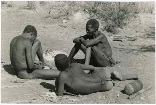 "/Qui Navel" making arrows by a fire and an unidentified person and "Old Gau" seated to the right watching him (print is a cropped image)