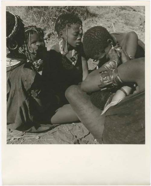 Group of women and girls sitting, and one woman fixing another woman's earring