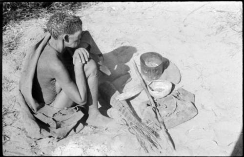 //Ku≠tera sitting with her few possessions, including a sewn leather bag, roasted melon seeds in a dried melon, digging stick, fire paddle, sieve, and a shoulder bag