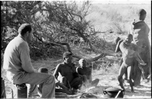 Oukwane sitting by his fire, a boy carrying N!whakwe nearby, and William Donnellan sitting and watching them