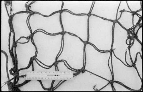 Section of carrying net belonging to /Twikwe's husband, with a ruler for measurement