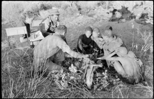 Oukwane and other people sitting and talking to William Donnellan and Elizabeth Marshall Thomas, with Wilhelm Camm interpreting. Oukwane is naming the internal parts of an animal.