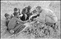 Oukwane and other people sitting and talking to William Donnellan and Elizabeth Marshall Thomas, with Wilhelm Camm interpreting. Oukwane is naming the internal parts of an animal.