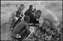 Oukwane and other people sitting and talking to William Donnellan and Elizabeth Marshall Thomas, with Wilhelm Camm interpreting. Oukwane is naming the internal parts of an animal.