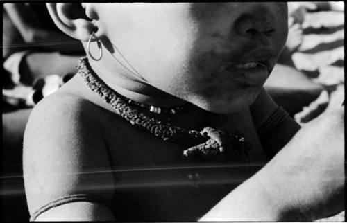 N!whakwe wearing a necklace and earring, close-up