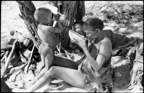 DaSi!Na and N!whakwe drinking, with Tsekue reclining in the background