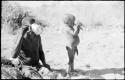 !Gai and N!whakwe each drinking respectively from a tin and a bowl