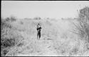 N!whakwe standing in the grass drinking from a tin