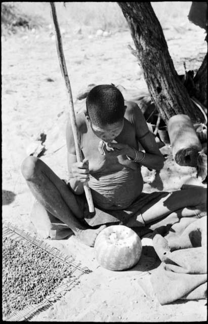 /Twikwe eating a piece of tsama melon, with a pile of seeds on a mat on the ground near her