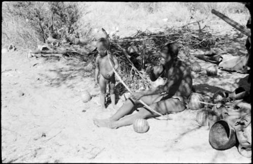 !Gai sitting in his place in the werft and holding a bow, with N!whakwe beside him