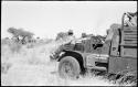 Children riding on the top of an expedition truck (GMC), and Wilhelm Camm riding on the fender, with a group of people standing under a tree in the distance