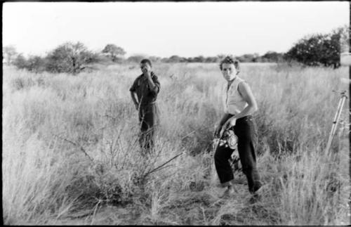 Kernel Ledimo and Elizabeth Marshall Thomas standing in the grass; Elizabeth holding a movie camera