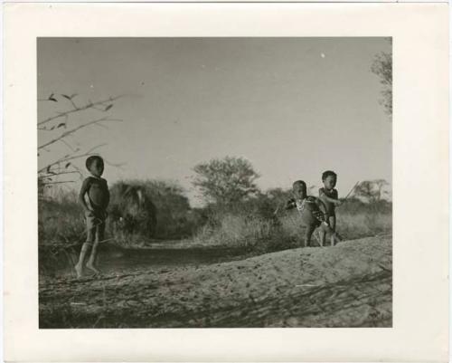 /Gaishay and "Little Gao" playing the stick-throwing game, standing on an ant-hill, with another boy standing near them (print is a cropped image)