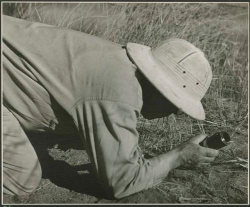 Laurence Marshall kneeling on the ground and holding a camera lens (print is a cropped image)