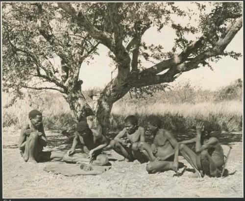 Group of men sitting under a big tree, throwing and watching oracle disks, close-up of throwing (print is a cropped image)