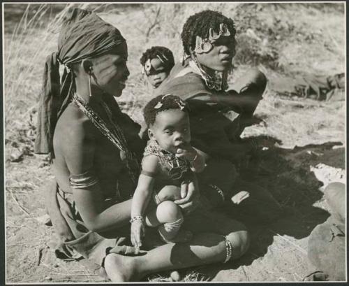 !Ghia of Band 10 sitting and holding her child, with another woman from Band 9 or 10 sitting next to her with her child (print is a cropped image)