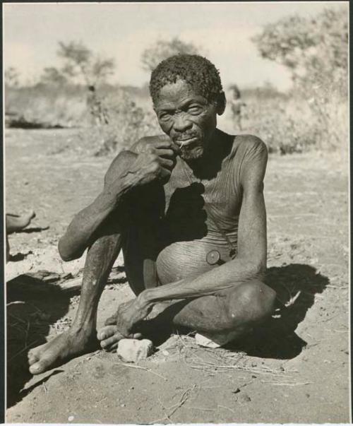 Man sitting and resting his leg on a stone, possibly Gao of Band 10 or //Ao (print is a cropped image)