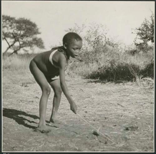 Boy picking up a djani (helicopter toy / winged toy made from a hollow reed) with his stick  (print is a cropped image)