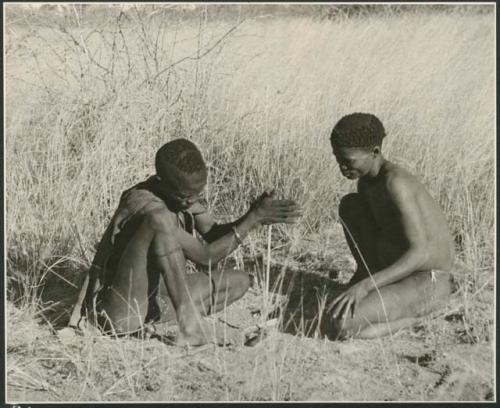 ≠Gao (headman of Band 3) and "/Qui Hunter" (≠Gao's sister's husband) starting to make fire. ≠Gao is beginning to twirl the "male" stick in the notch of the "female" stick which he steadies by pressing it down with his digging stick and his foot. (print is a cropped image)