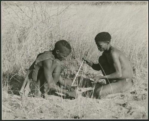 ≠Gao (headman of Band 3) and "/Qui Hunter" (≠Gao's sister's husband) starting to make fire, with ≠Gao placing the tinder on the ground (print is a cropped image)