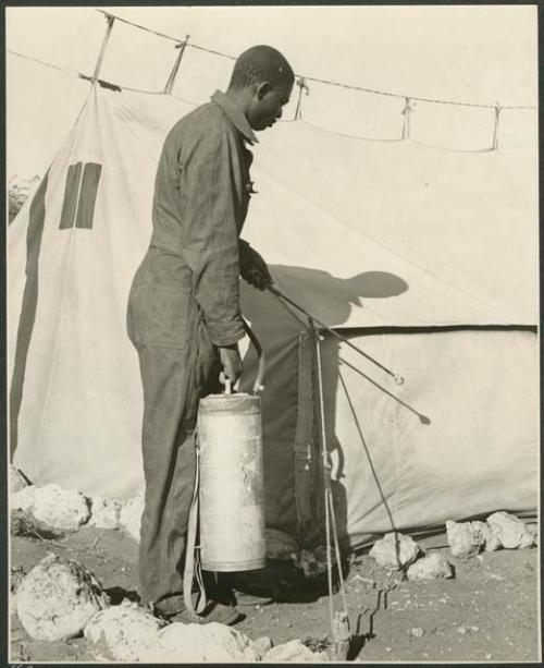 Expedition staff member spraying DDT beside a tent (print is a cropped image)