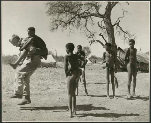 Group of boys playing with John Marshall, including /Gishay (son of "Old Gau") on his back, ≠Toma (son of Gau)  facing the camera, and !Naishi and //Ao (son of "Old ≠Toma" of Band 2) standing to the right (print is a cropped image)